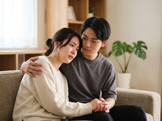 Fototapeta premium 白いニットの女性を抱き寄せ落ち着いたトーンの部屋で見守る男性