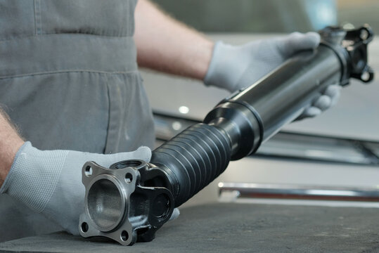 Auto parts.Replacing the driveshaft. An auto mechanic holds in his hands a new cardan shaft with a crosspiece.Checks the serviceability and prepares the product for installation.