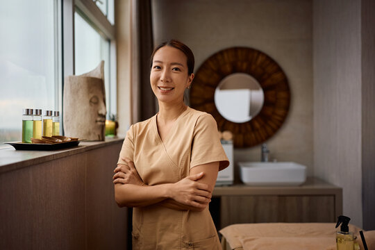 Smiling Korean wellness therapist standing with her arms crossed and looking at camera.