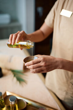 Close up of wellness therapist preparing massage oil for relaxing massage at spa.