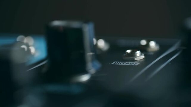 Close up musician hand unplugging audio jack cable from output guitar effects pedal, disconnecting sound equipment in dark music studio setting. Musician unplugging jack cable from guitar effect pedal