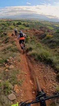Mountain bikers riding narrow dirt trails along a scenic high ridge in this thrilling action footage captured from a first person perspective on a summer day