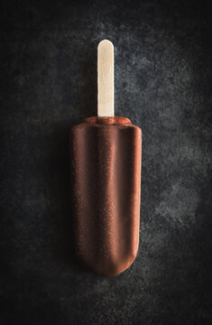 Single chocolate ice cream bar on dark surface from above