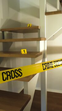 Domestic crime scene investigation inside a home, showing yellow police tape cordoning off a modern wooden staircase with evidence markers placed on the steps, indicating forensic examination