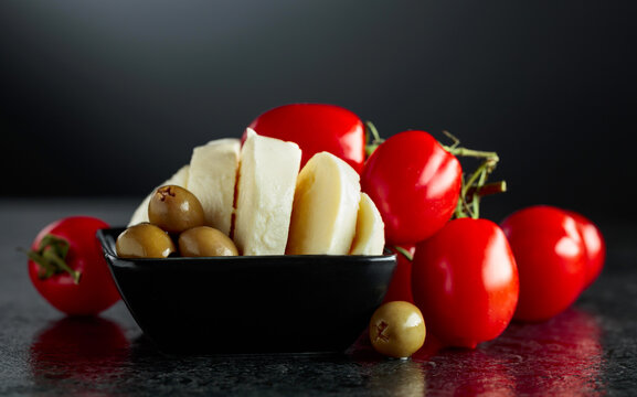 Mozzarella with green olives and red cherry tomatoes on a black stone table.