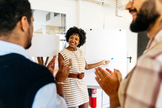 Diverse business professionals applauding smiling african american woman presenting on whiteboard during a coworking space meeting