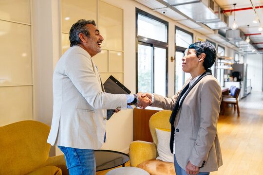 Two diverse business people shaking hands in a modern coworking office, establishing partnership and agreement