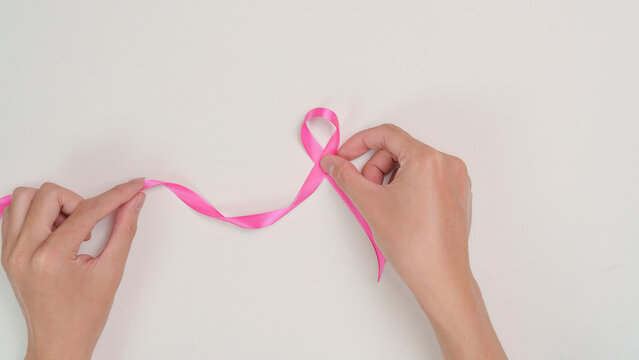Cropped hands folding pink ribbon on white background for breast cancer awareness campaign