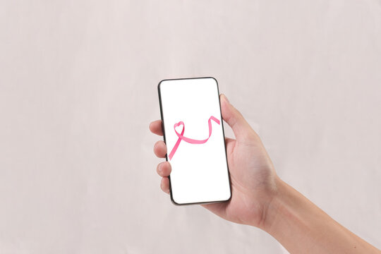 Cropped hand holding smartphone displaying pink ribbon for breast cancer awareness