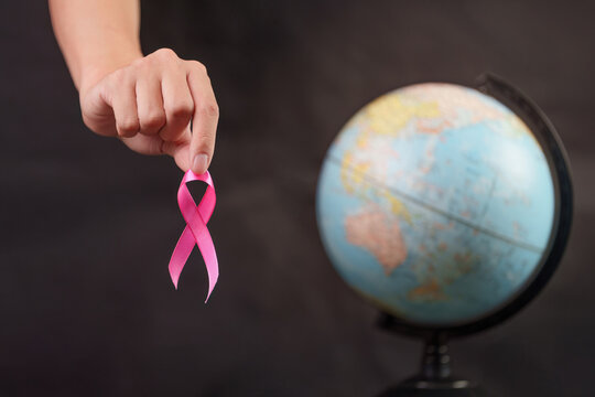 Cropped hand holding pink ribbon with globe for global breast cancer awareness
