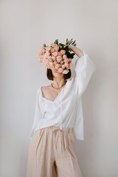 Woman in beige outfit holding blooming roses for artistic portrait session. Soft colors and floral fashion aesthetics