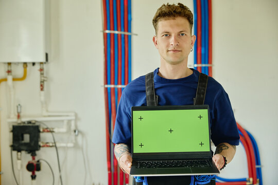 Portrait of young adult Caucasian male plumber holding laptop with green screen during house renovation. Image ideal for promoting smart home installation services, medium shot