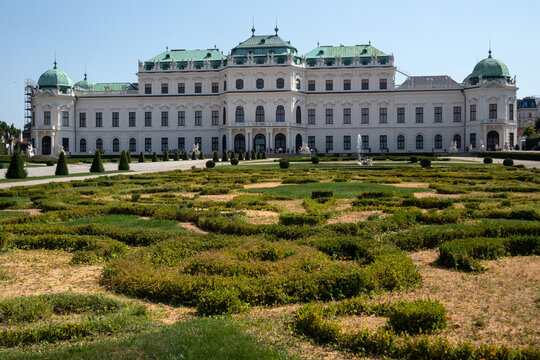 Facciata esterna del Palazzo del Belvedere Superiore con i monumentali giardini barocchi geometrici in primo piano sotto un cielo azzurro, famosa attrazione turistica e storica di Vienna, Austria.