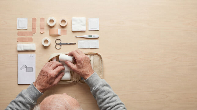 Senior man organizing bandages thermometer medical supplies inside first aid kit, authentic active aging concept showing independence daily value value value value value value value