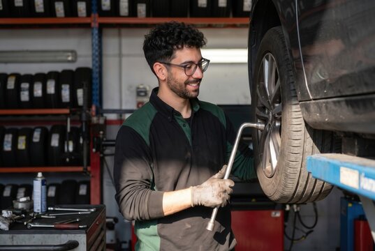 Young male automotive technician working on a hoisted car wheel