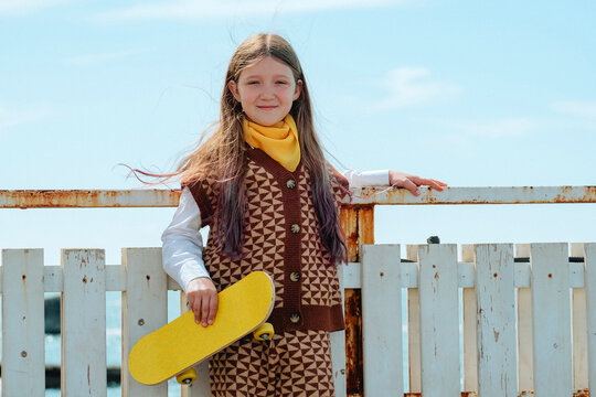 Smiling girl holds a yellow skateboard by the sea