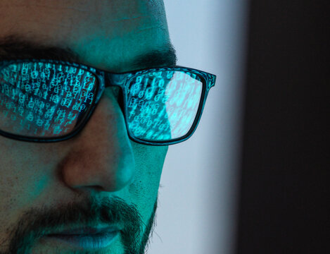 Hacker wearing eyeglasses with reflection of binary codes