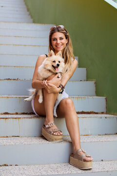 Smiling young woman sitting on stairs holding her dog