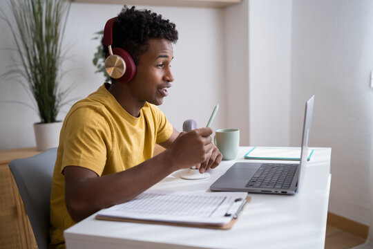 Man speaking into microphone with headphones at laptop in home office