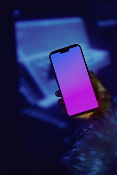 Hand holding glowing smartphone mockup in neon nightclub