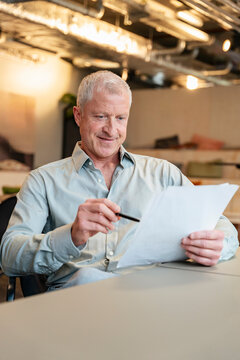 Smiling businessman reads a document at his modern office desk
