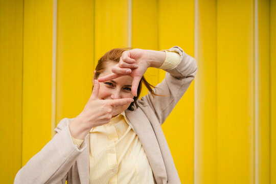 Businesswoman making framing gesture against yellow background
