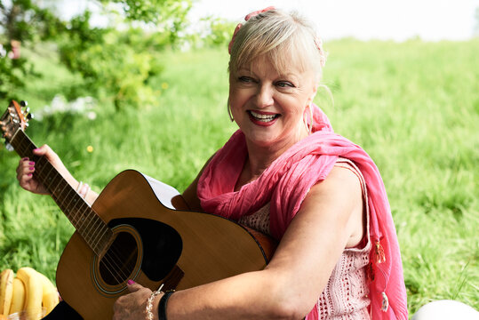 Portrait of happy senior woman playing guitar in park