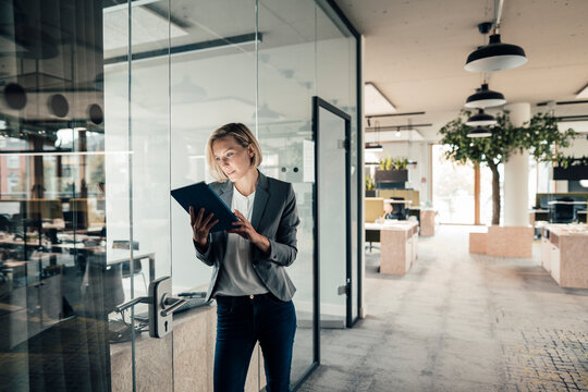 Female entrepreneur using digital tablet while leaning on glass wall