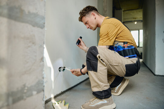 Young adult Caucasian male electrician installing wiring in wall during house renovation. Image suitable for home improvement services and construction marketing campaigns
