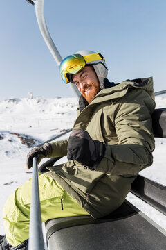 Happy young man gesturing with closed fist sitting on ski lift