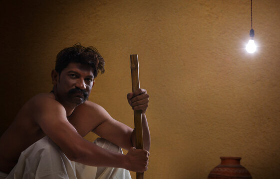 Portrait of rural Indian man sitting indoors holding stick