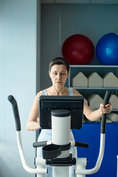 Mature woman uses an elliptical machine for physiotherapy indoors