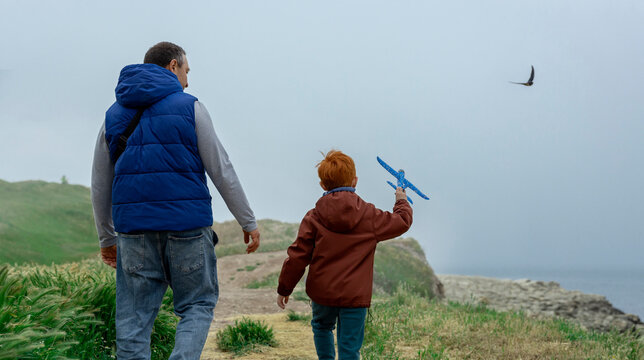 Father and son walking outdoors near the sea holding a toy plane