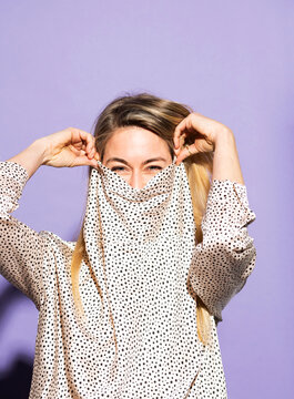 Woman hiding face with polka dot shirt against purple background