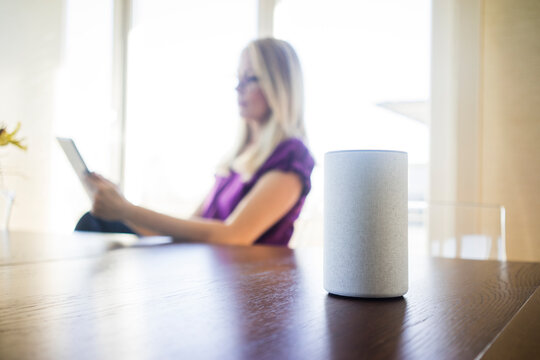 Smart Home loudspeaker on table with woman using tablet in the background