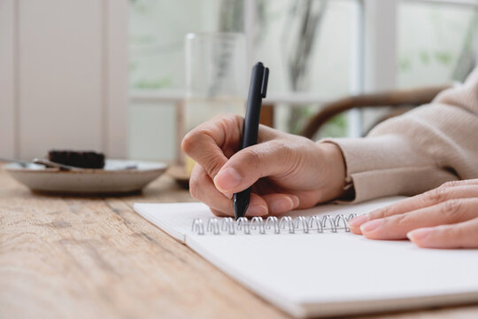 Close-up of a hand writing in a spiral notebook on a wooden desk. Ideal for education, planning, journaling, productivity, business and lifestyle concepts.