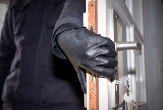 Male thief in black glove opens home door during daytime burglary