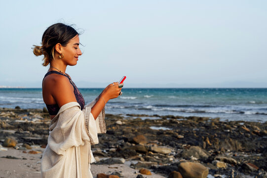 Smiling woman using mobile phone at beach