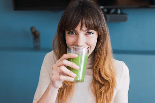 Smiling woman drinking detox juice at home