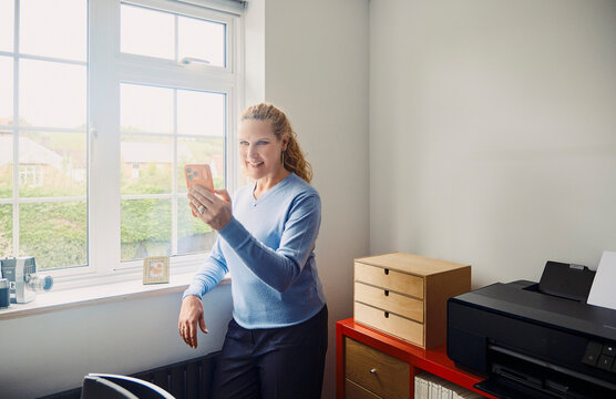 Smiling woman has a video call on phone in her home office