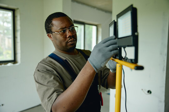 African American young adult male contractor adjusting construction spotlight during house renovation. Image suitable for home improvement services and professional trade marketing