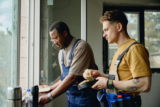 Diverse young adult male construction workers taking lunch break during house renovation. Image suitable for labor industry marketing and home improvement services, medium shot
