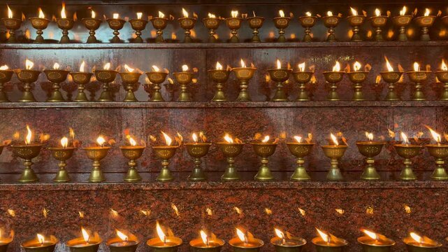 Rows of illuminated butter lamps burning inside a Buddhist temple, symbolizing prayer, devotion and spiritual tranquility