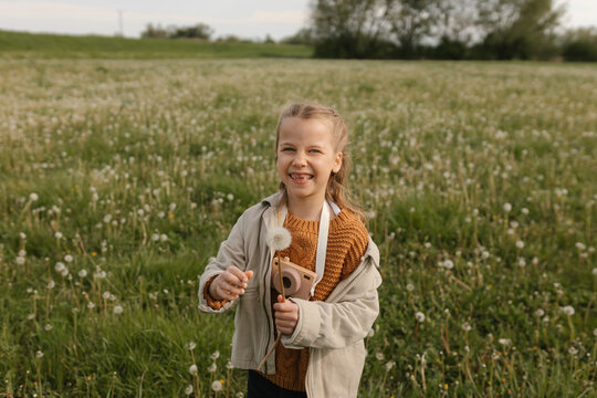 Happy girl holds a dandelion and toy camera in a spring field