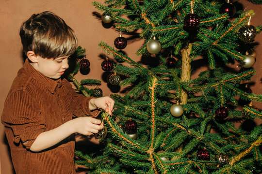 Boy decorating a Christmas tree with a bauble indoors at home