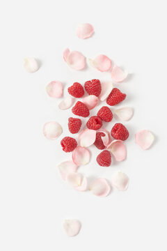 Fresh raspberries and rose petals against white background