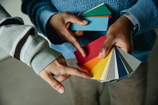 Diverse adult designers holding and pointing at color swatches, choosing palette for house renovation. Close up shot highlighting interior design planning and creative collaboration