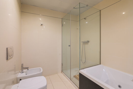 Modern neutral bathroom with glass shower enclosure, bathtub, and wall-mounted bidet in bright tiled interior, with bathroom, shower, bathtub, bidet detail, showing glass, tile, tiled, interior