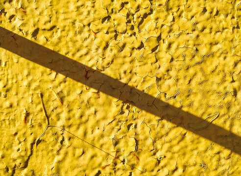 The background is made of metal and painted bright yellow. It has a rough, uneven, vintage texture with rust showing through. The shadow is diagonal and oblique.