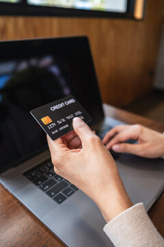 Close-up of a person holding a credit card while using a laptop for online shopping. Concept of e-commerce, digital payment, online banking and secure transactions.